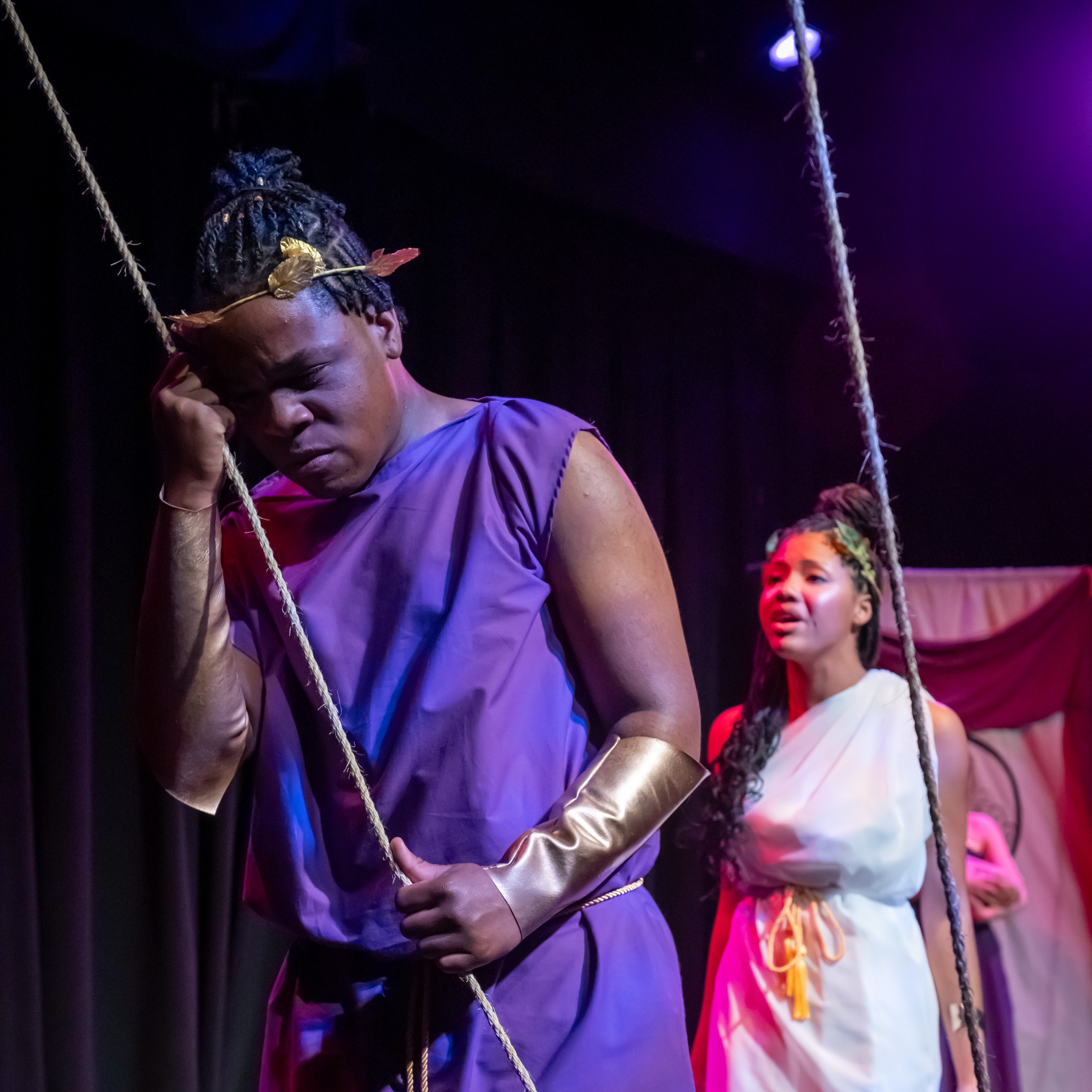 A man stares off to our right, leaning on a rope. a young woman behind him looks at him